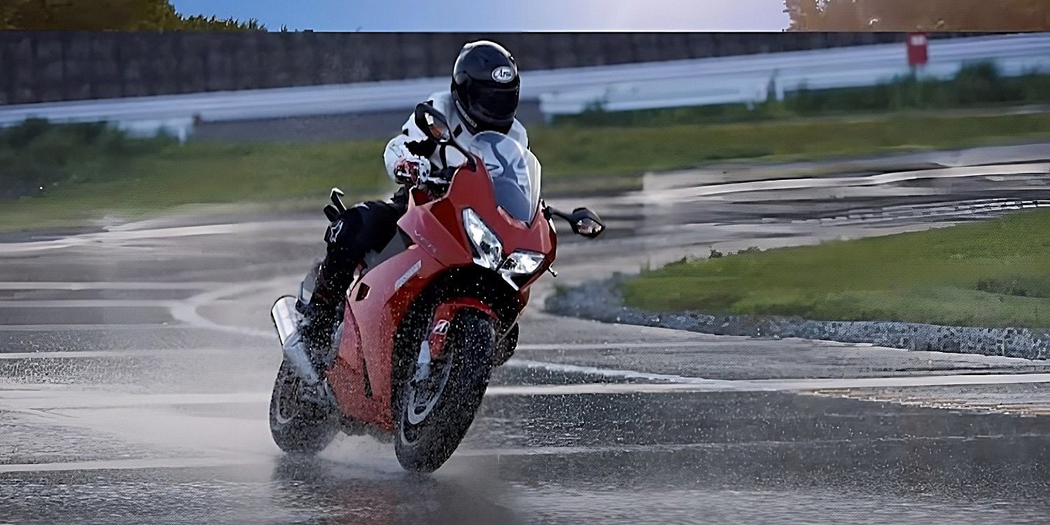 Leaning a red Ducati sport bike during cornering on a wet track. It's a delicate balance leaning and counterbalancing to manage taking the corner at considerable speed with the reduced traction. Leaning the bike too much in the rain will have you lose the rear.