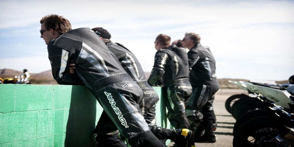Five instructors from the California Superbike School, dressed in AGVSPORT leather suits (including the AGVSPORT Monza Race Suit), watch their students ride while their bikes are parked in the background. Wearing the suit regularly can help break it in faster.