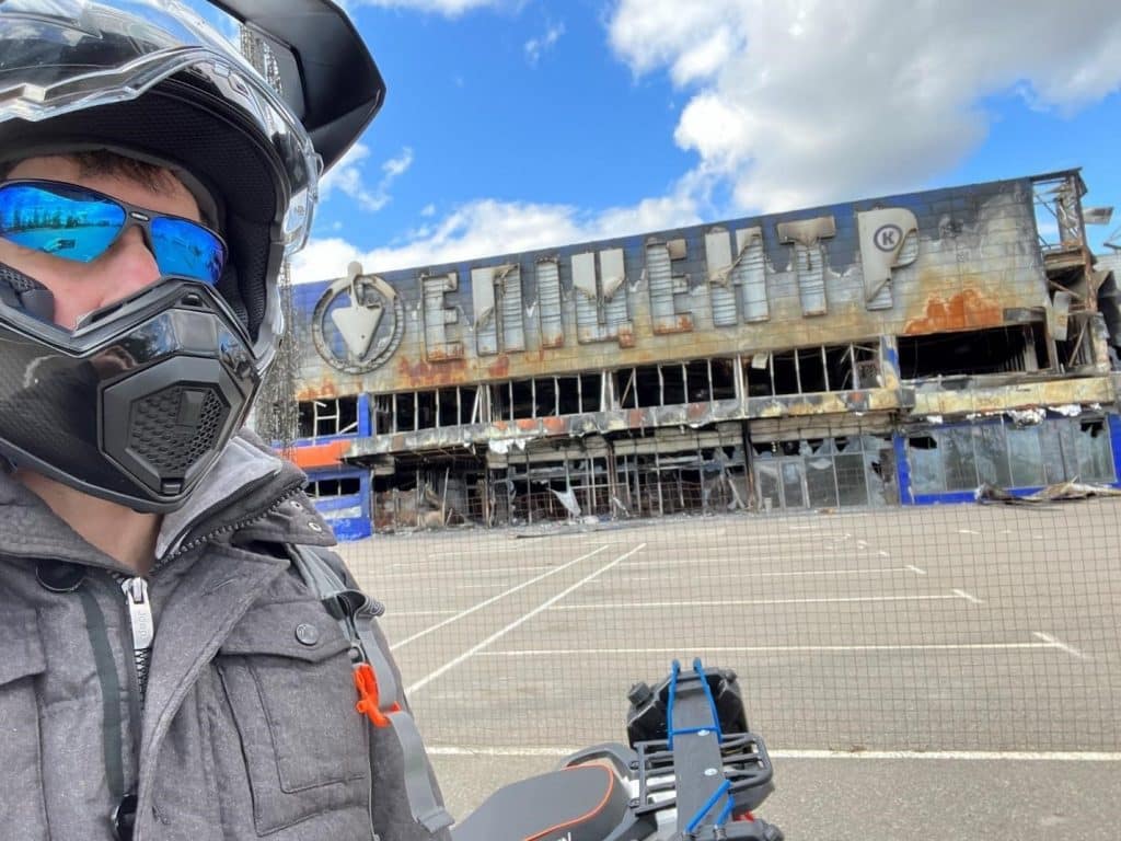 Last fall in Bucha, Ukraine, I’m standing in front of Epicenter (similar to Ukrainian Home Depot), next to my Tekken 250 Adventure Touring bike, wearing my AGV AX9 Carbon helmet with the visor open and my glasses on.