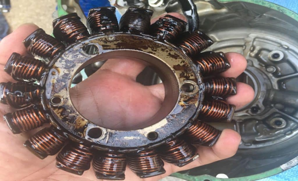 Inspecting a motorcycle stator for damage. In this design, the stator bathes in engine oil, but damage is clearly visible on the blackened upper coils.