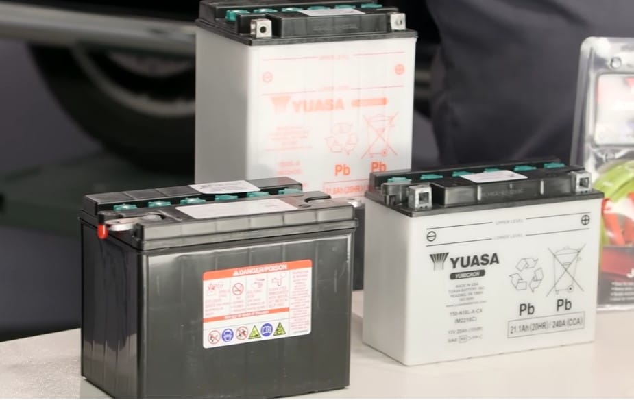Three Yuasa wet cell lead-acid batteries with labels showing the maximum and minimum electrolyte levels through the translucent casing.