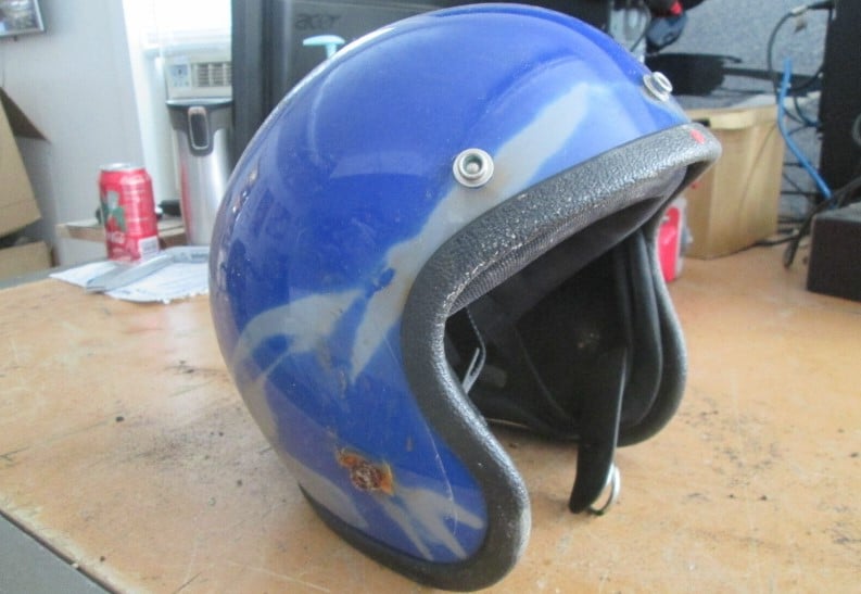 Worn out open face helmet shows signs of sun exposure damage with streaks of faded paint and rusty metal appendages.