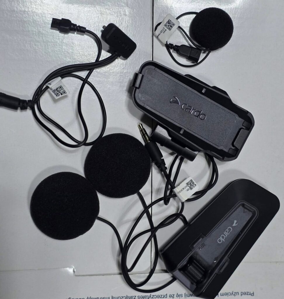 Top 5 Best Motorcycle Helmet Bluetooth Headsets for Music Cardo motorcycle intercom kit with mounting clip, two foam-covered helmet speakers connected by wires, a small wired microphone and 3.5mm connector.