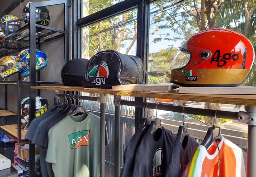Display at the AGV Helmet Thailand store featuring an array of items, including t-shirts, a variety of full-face helmets such as multiple models of Valentino Rossi helmets and the AGV X3000 Helmet, along with helmet bags. While the helmets are strategically positioned near the window for marketing purposes, it's important to note that exposing your helmet to direct sunlight during storage is not advisable.