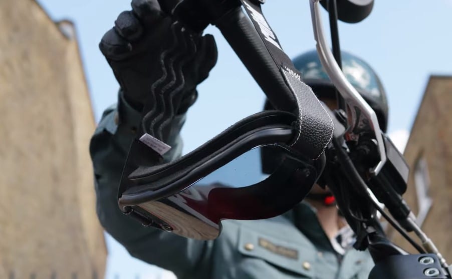Goggles elegantly suspended from a motorcycle handlebar, poised for immediate use with an open face helmet.