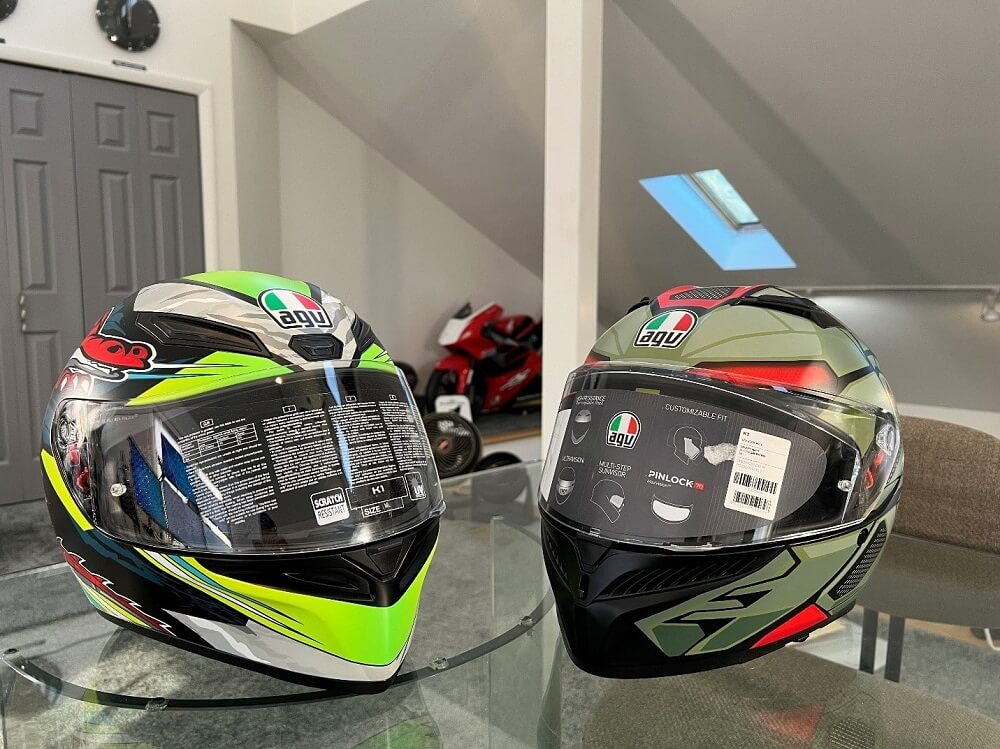 In my AGV Sports Group Office in Frederick, Maryland, the AGV K1 Dundee Matte Lime Red helmet sits on the left, while the AGV K3 Decept Matte Black/Green/Red occupies the right. In the background, you can spot my Honda RS125R, a 125cc two-stroke Grand Prix racing bike.