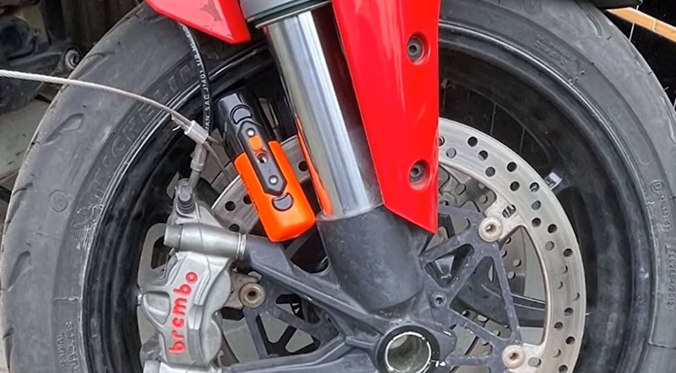 The Kryptonite Evolution Compact Disc Lock in vibrant orange securely fastens through the rear disc rotor, effectively preventing the motorcycle from being wheeled away while it's in place