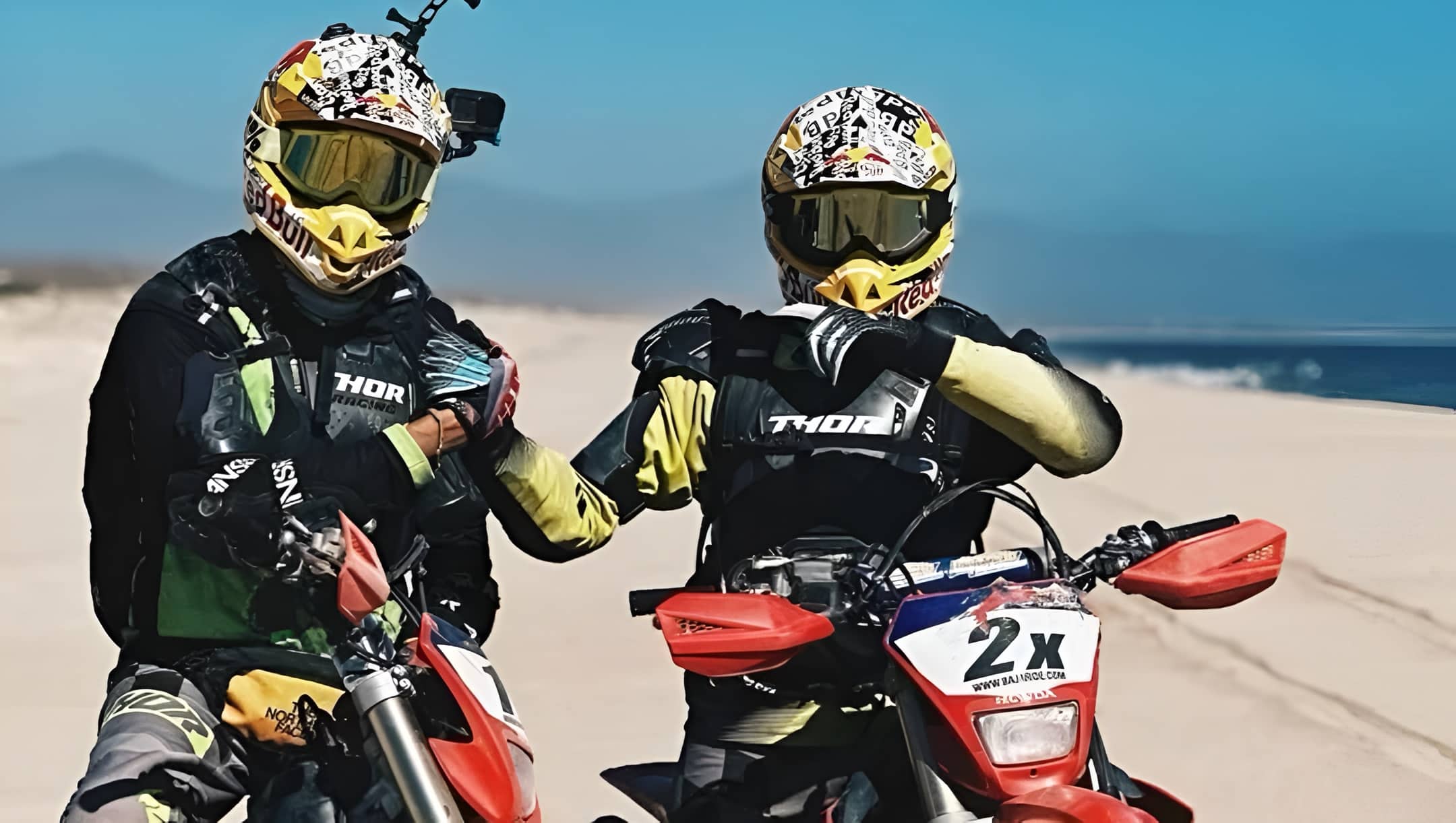 Two motorcyclists posing with their dirt bikes on a sandy trail, greeting each other with a friendly handshake reminiscent of the camaraderie often shared among riders in Vietnam’s touring culture, where brotherhood and mutual respect on the road are deeply valued.