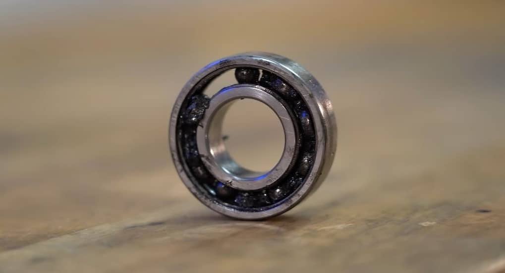 A damaged motorcycle wheel bearing with missing and worn-down balls, dried contaminated grease, and visible scoring on the inner and outer race.
